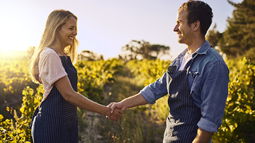 A man and a woman wearing aprons over their clothes and shaking hands