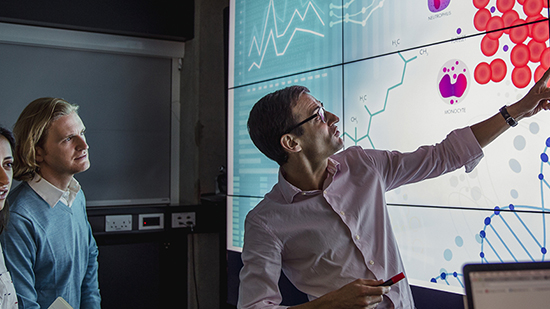 Man pointing at a screen showing DNA with colleagues watching