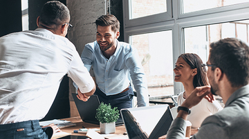 Group of colleagues having a meeting, two people are standing up to shake hands